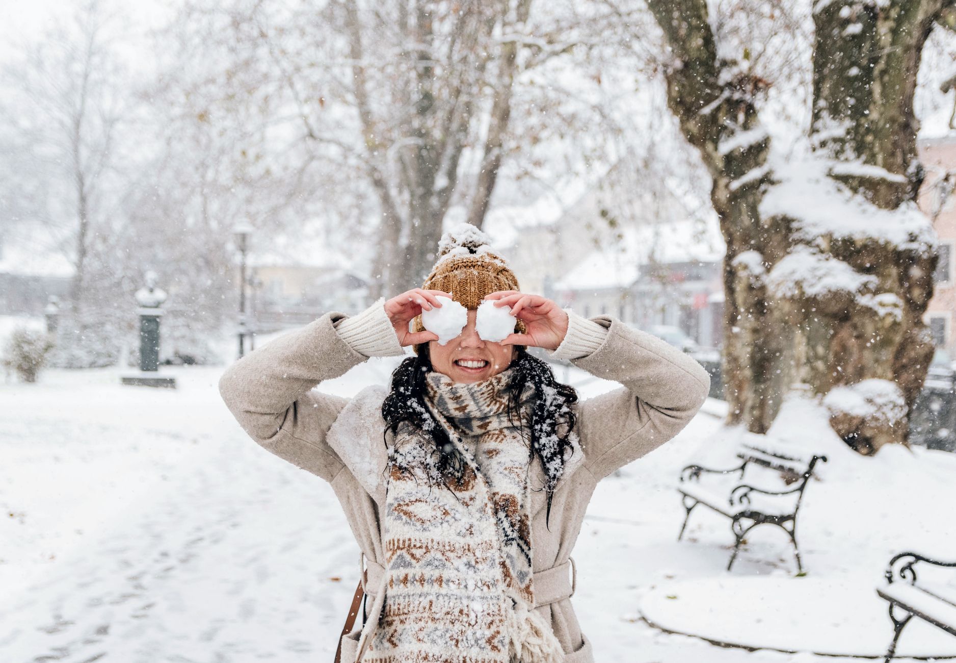 Woman enjoying a snowy winter day by playfully holding snowballs in a park.