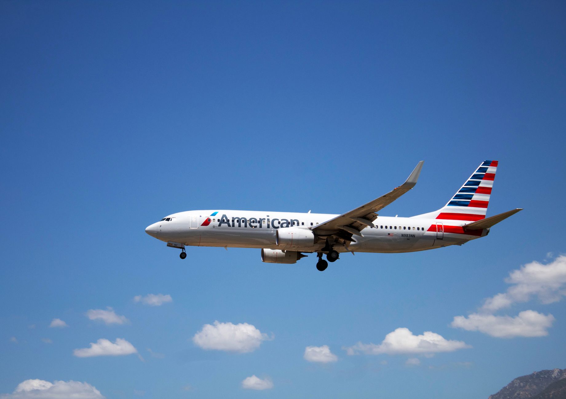 An American Airlines plane flying through a clear blue sky, showcasing aviation travel.