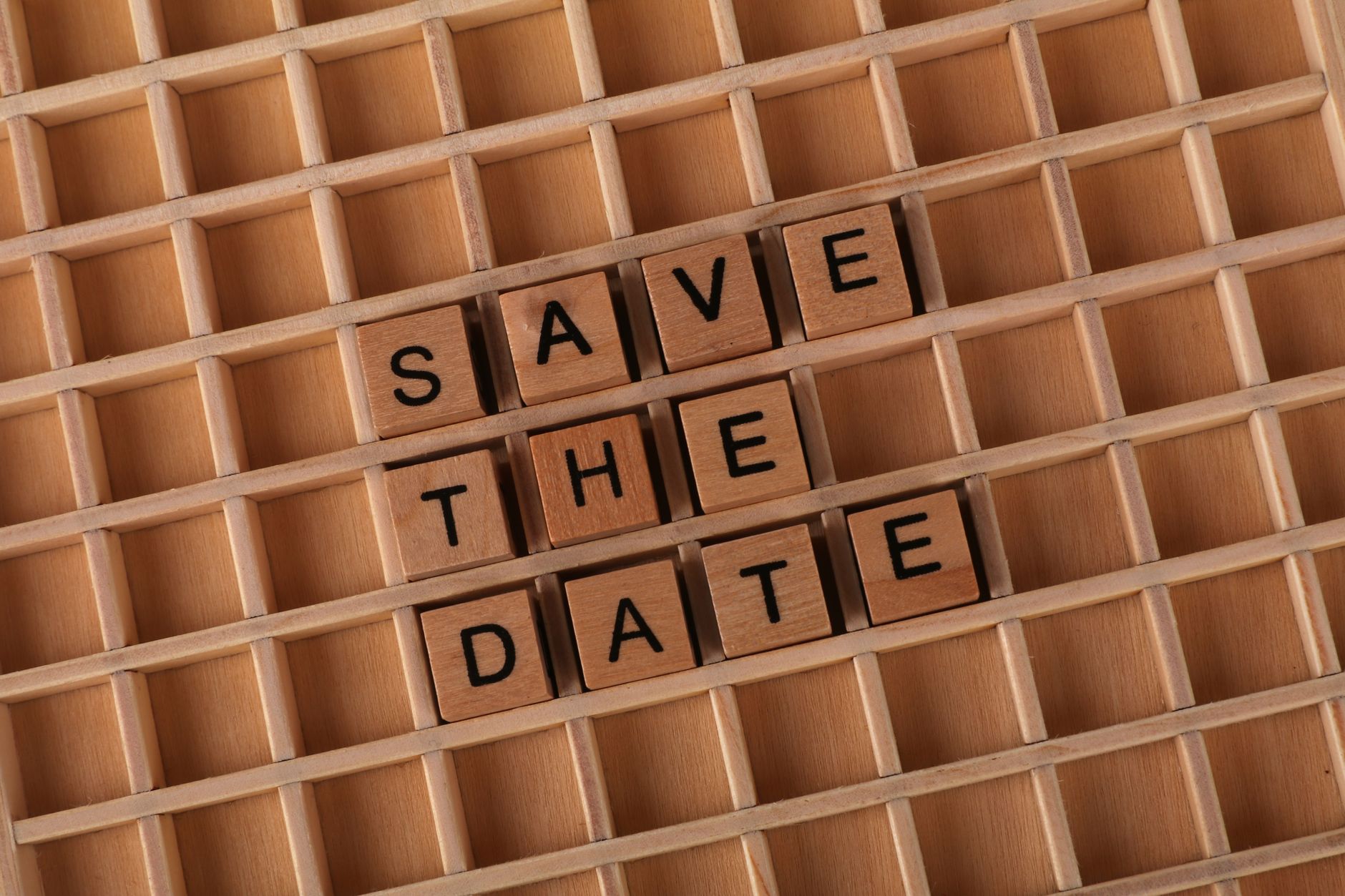 Top view of 'Save the Date' message using wooden letter blocks on a grid pattern background.