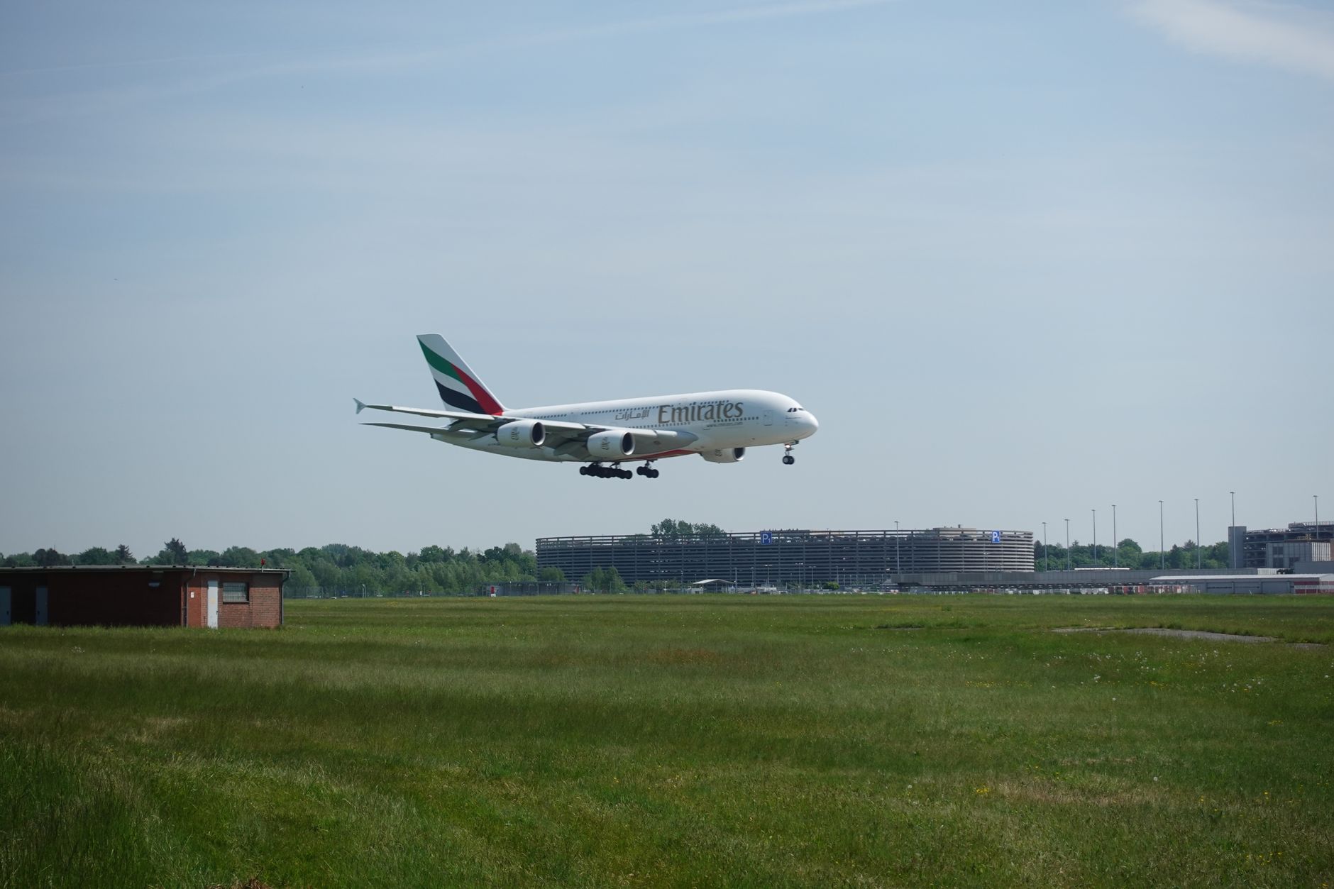 An Emirates Airbus A380 approaches landing at a bustling airport.