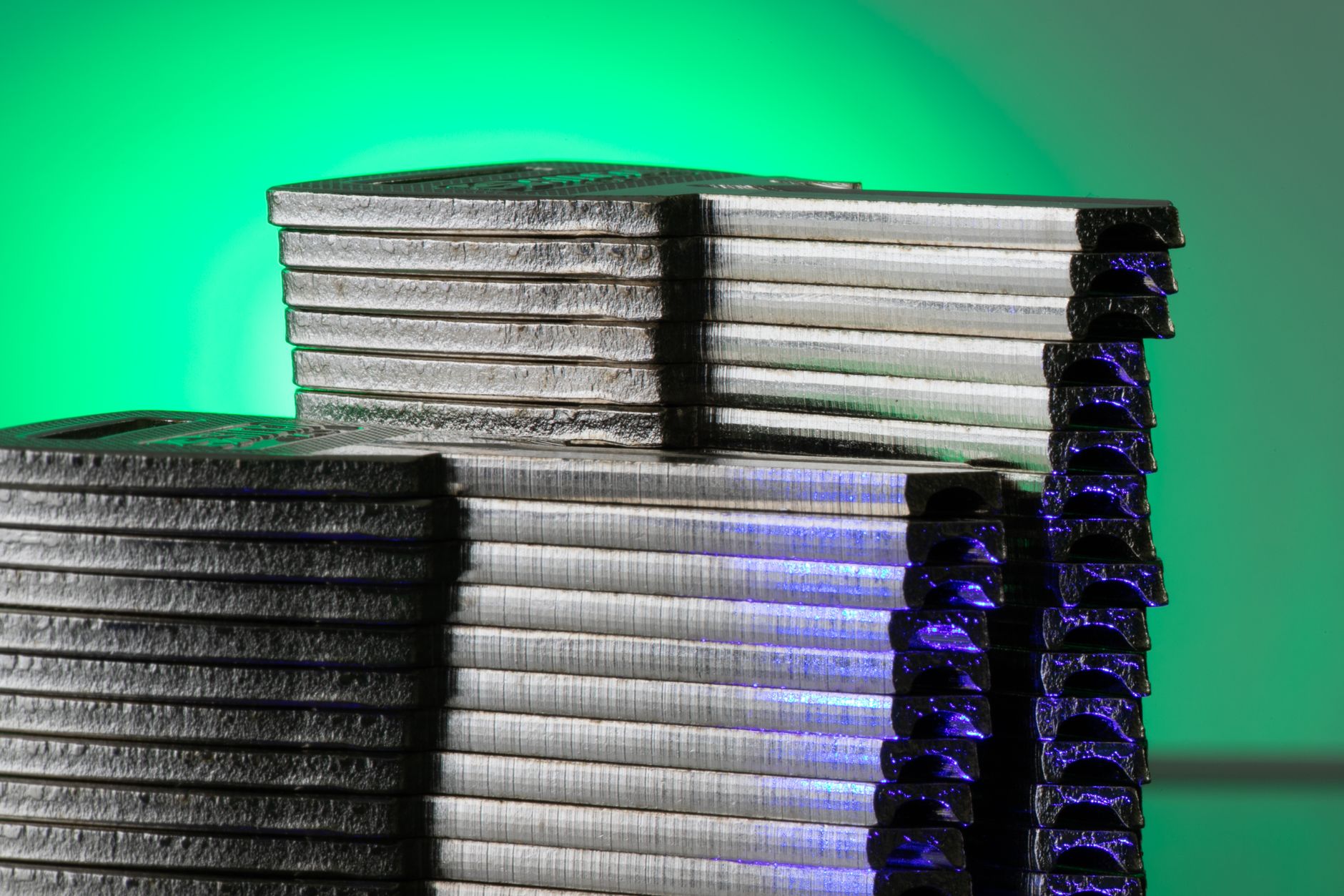 Close-up of stacked metallic discs reflecting green and blue light.