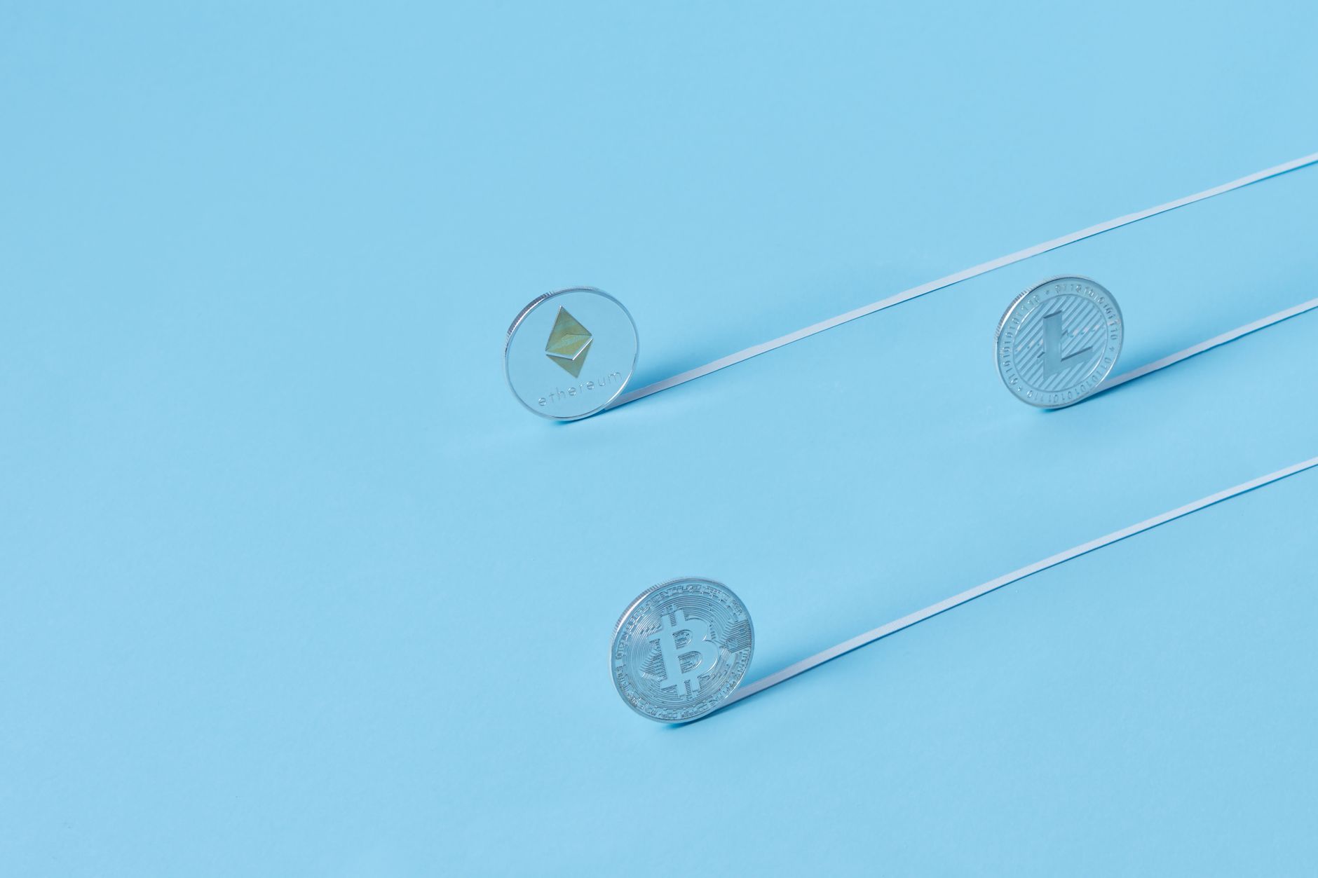 Minimalist image of Bitcoin, Ethereum, and Litecoin coins on a baby blue background.